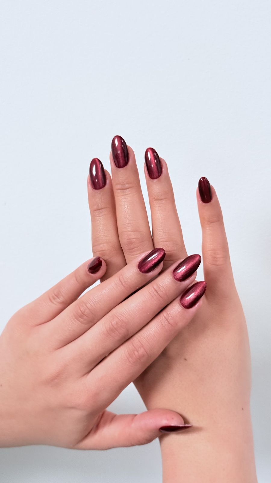 Handen met bordeauxrode chroomnagels in amandelvorm