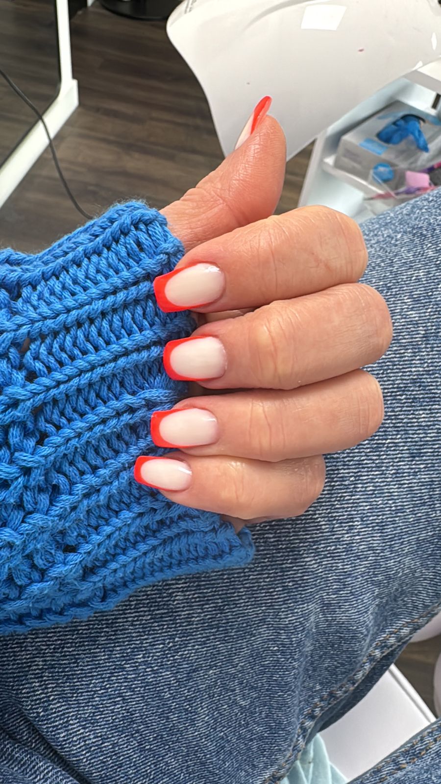 Nagels met een oranje French-rand tegen een blauwe gebreide mouw