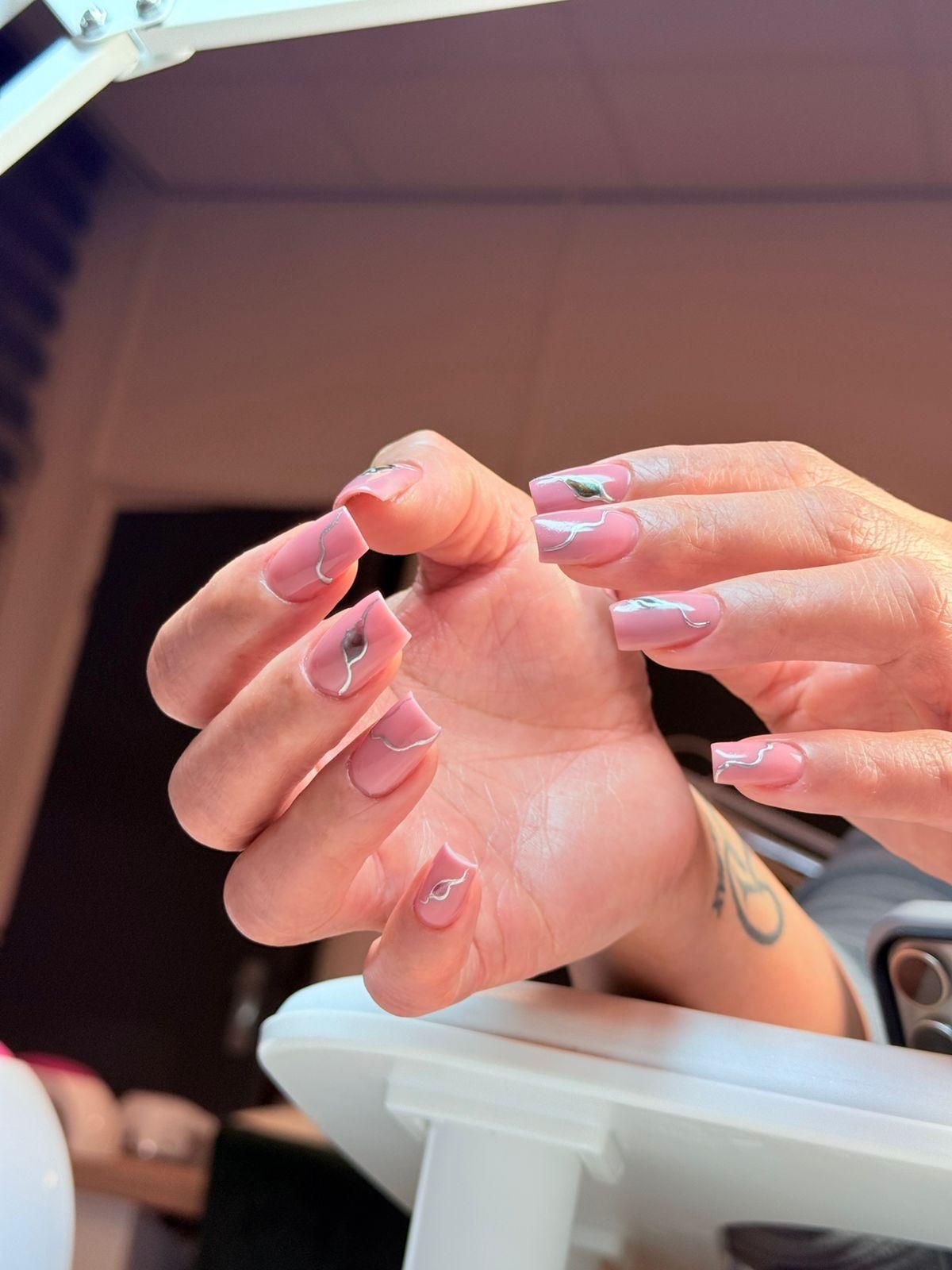 Roze vierkante nagels met zilveren lijntjes aan de manicuretafel