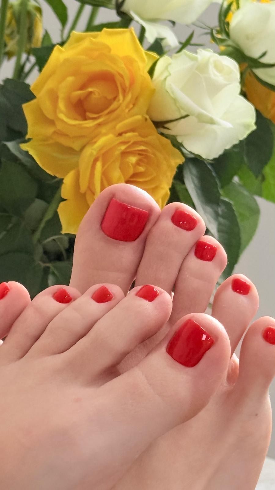 Teennagels met rode lak voor een bos gele en witte rozen